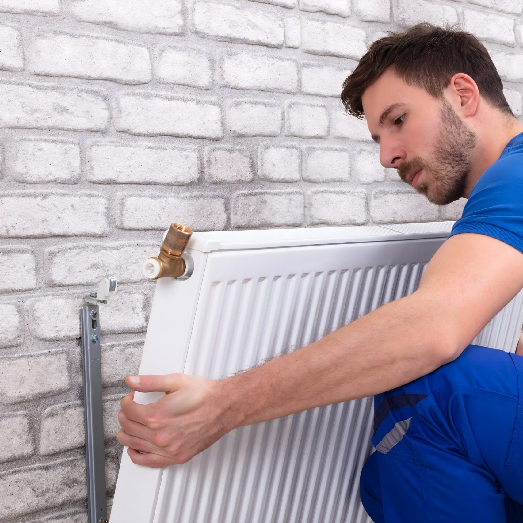 Young Repairman Installing Radiator On Brick Wall At Home